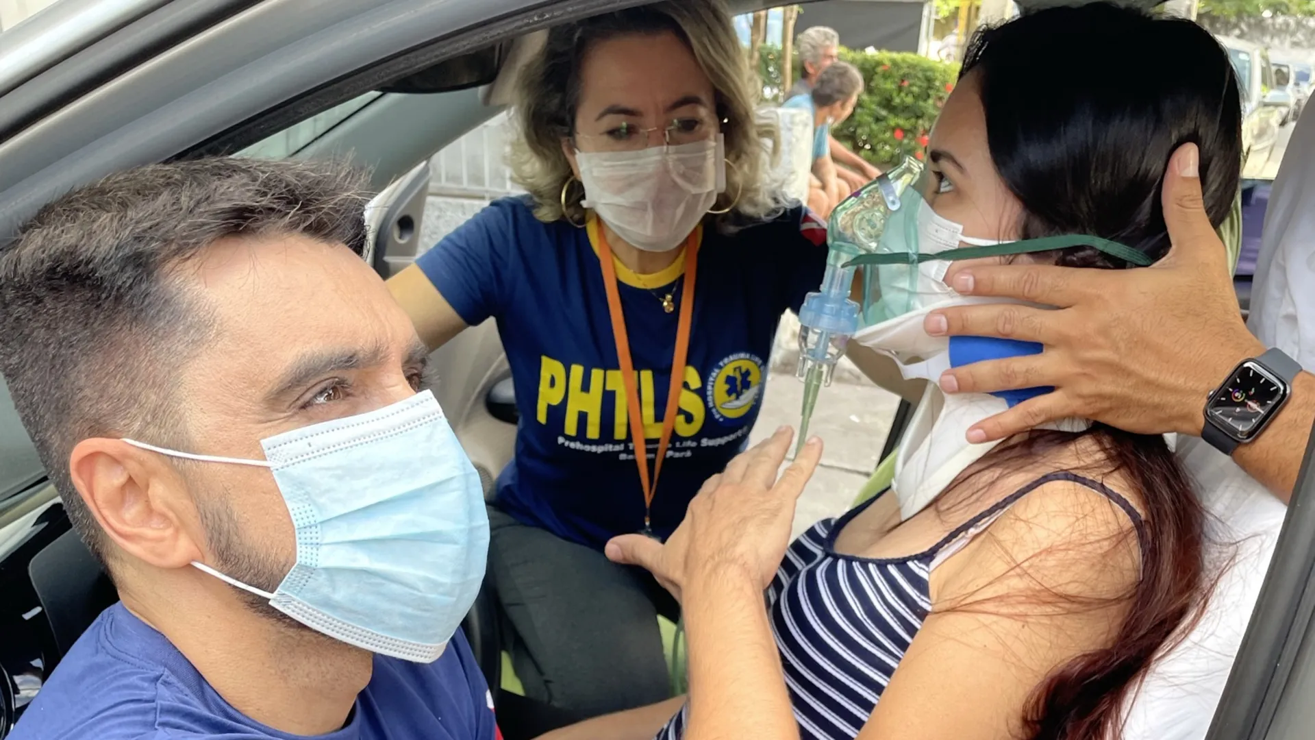 Instrutor do PHTLS estabiliza a cabeça de uma vítima simulada dentro de um carro, enquanto outra participante aplica oxigênio
