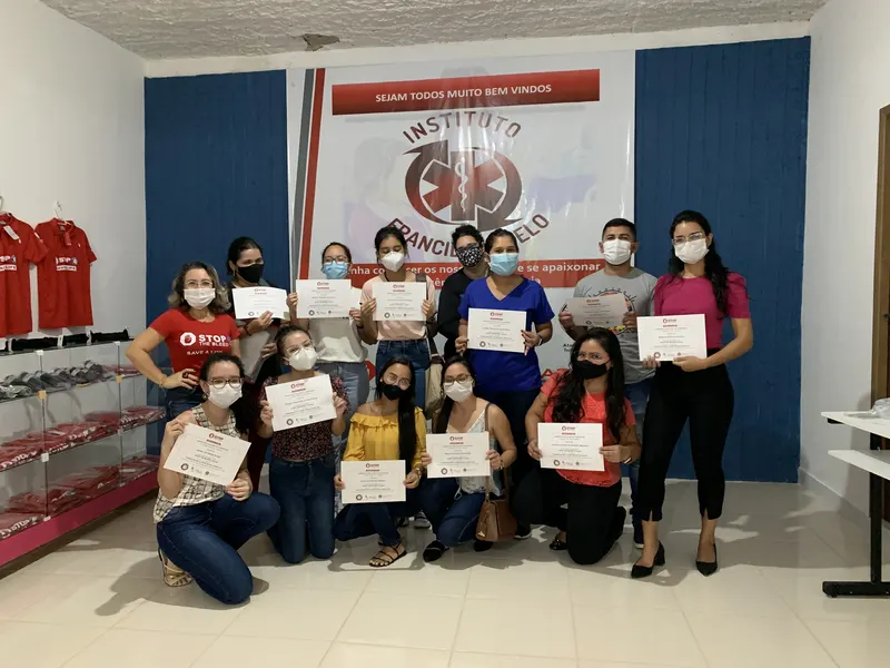 Turma reunida com os certificados em mãos, diante do painel do Instituto